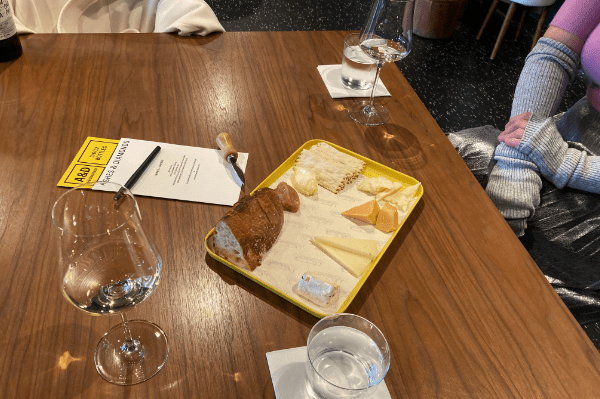 Ashes & Diamonds Wines & Cheese pairing table set. two glasses of white wine, cheese tray with focaccia bread and tasting menu.