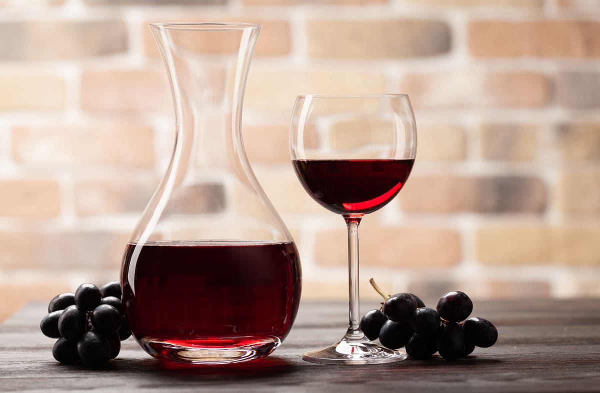 red wine in a wine glass and decanter next to grapes on table
