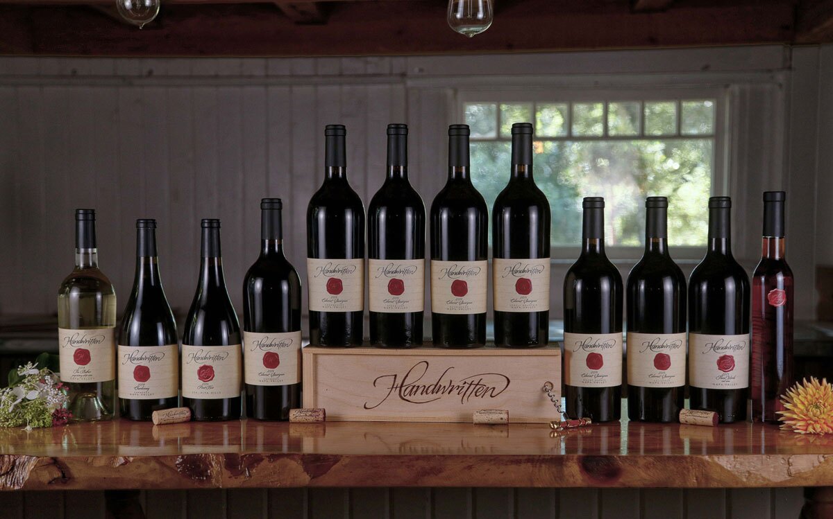 HandwrittenLineup_2016s Handwritten wine bottles arranged on a wooden table with a branded wooden crate in a tasting room setting